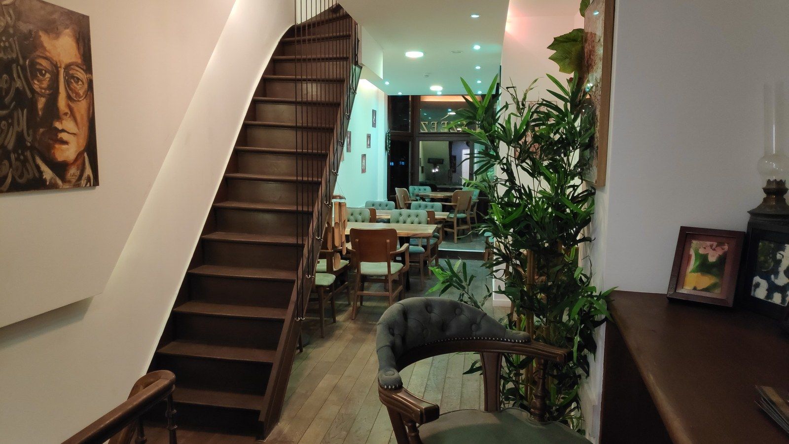 Salle du rez-de-chaussée avec escalier en bois, plantes et tableaux